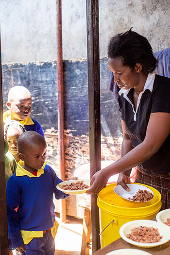 woman feeding stew to school kids