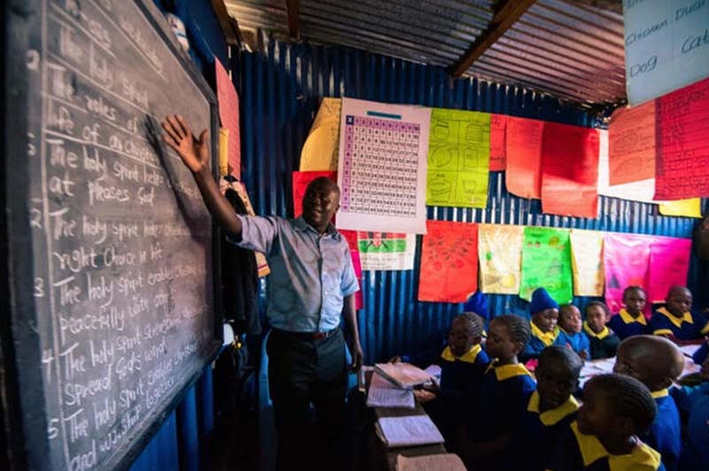 a teacher in kenya pointing to a lesson on a blackboard